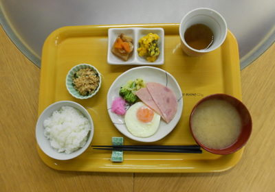 黄色いトレイに盛られた朝食セット。ご飯、味噌汁、目玉焼きなど一汁三菜の食事。